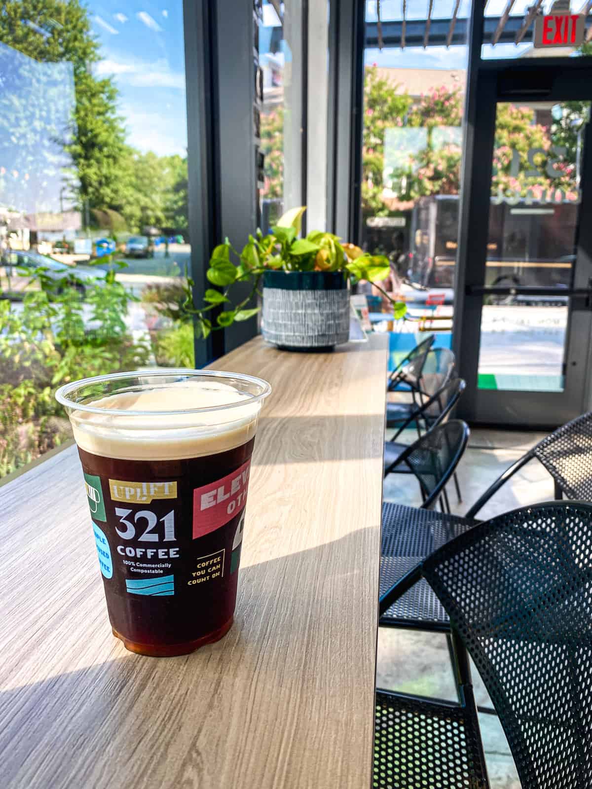 A plastic cup of nitro cold brew on a counter in a sunny coffee shop with lots of plans