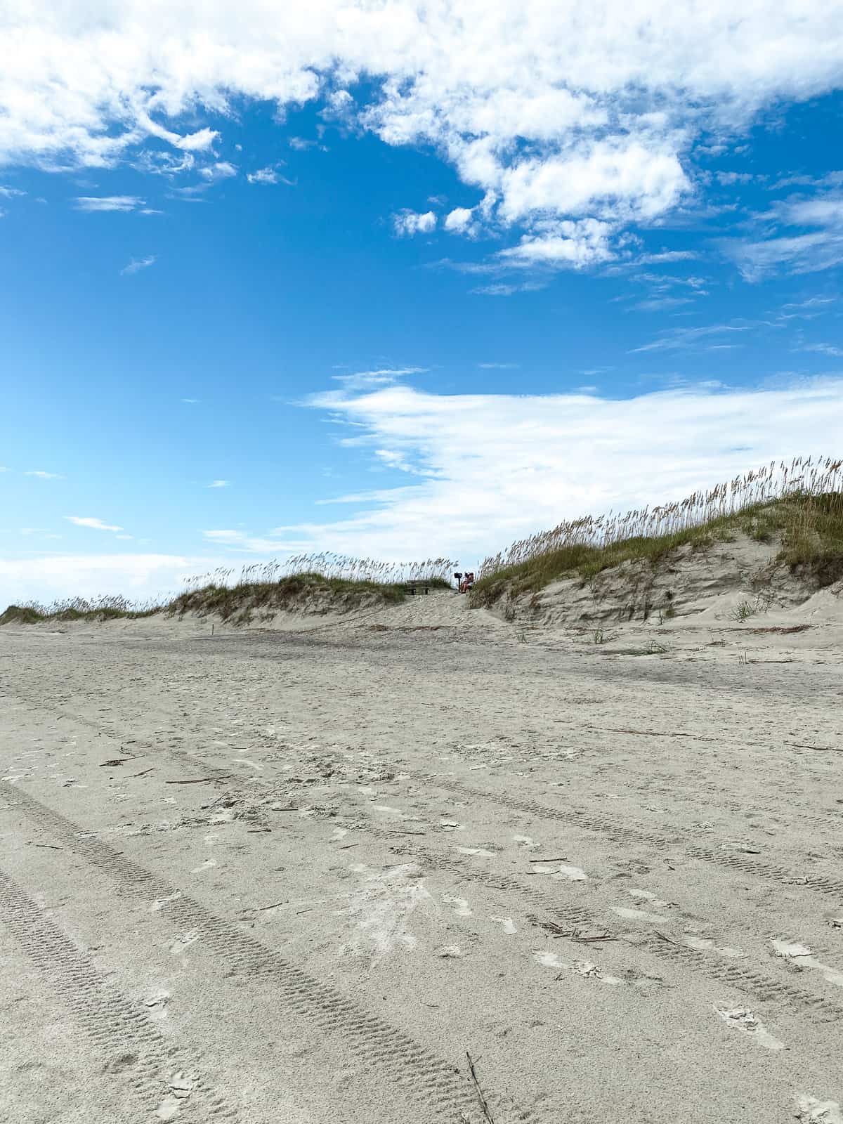 A bright blue skinny on Sunset Beach in North Carolina with some hills with grass blowing in the wind