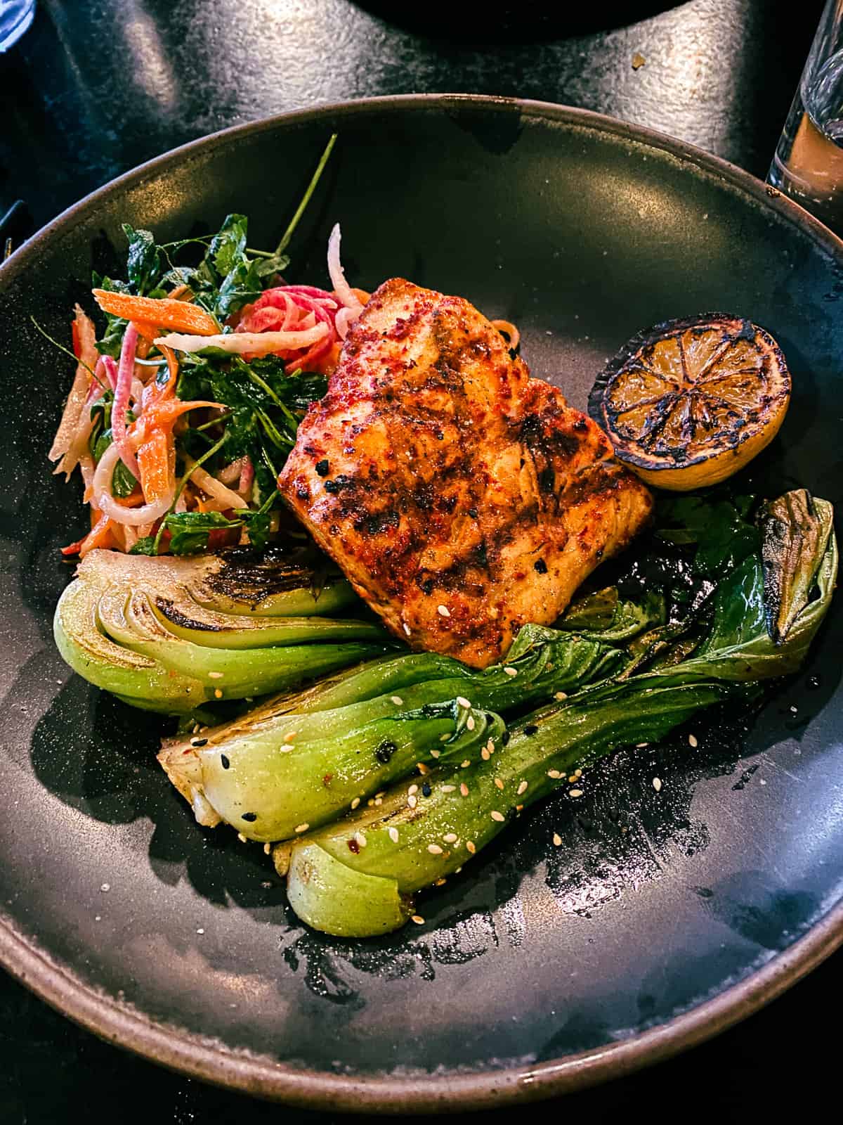 Mahi mahi with bok choy, charred lemon and a side salad on a modern black plate