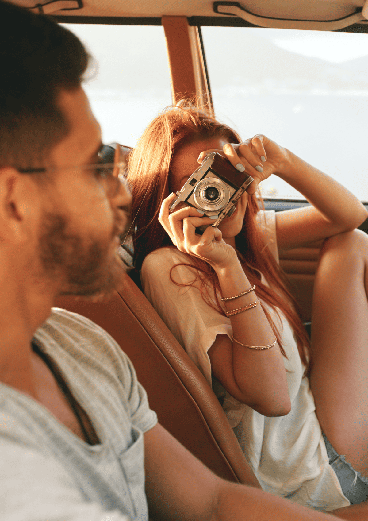 A couple sitting in a car and the woman is taking a photo of the man