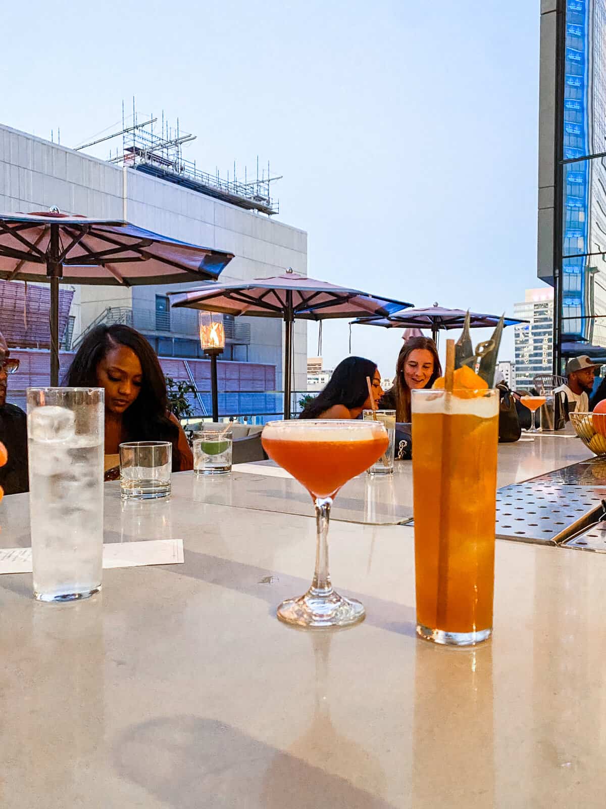 2 cocktails sitting on the counter at Aura rooftop in Charlotte NC. One is in a martini glass and one is in a tall glass.