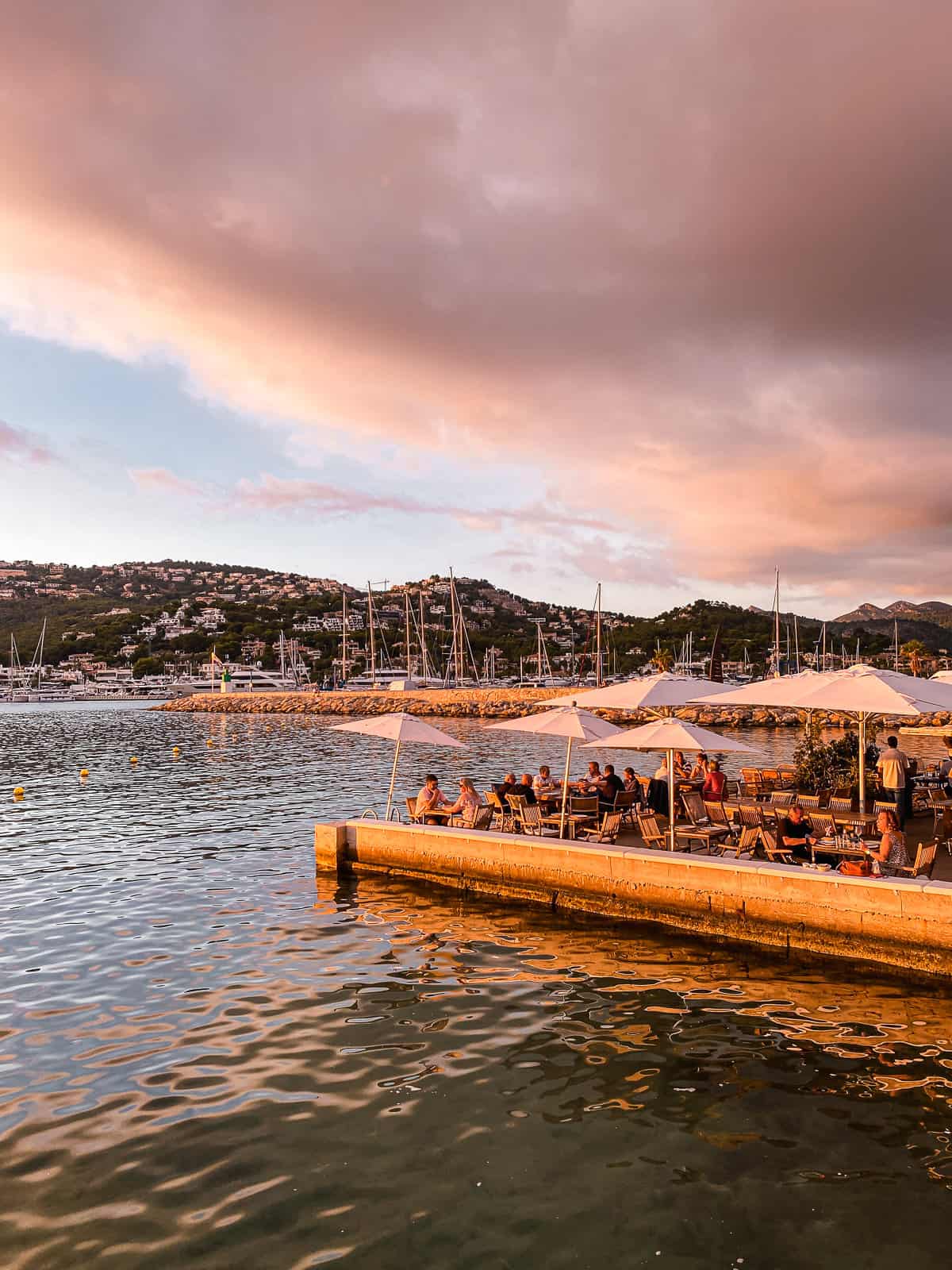 People sitting at a table on the side of the water at sunset