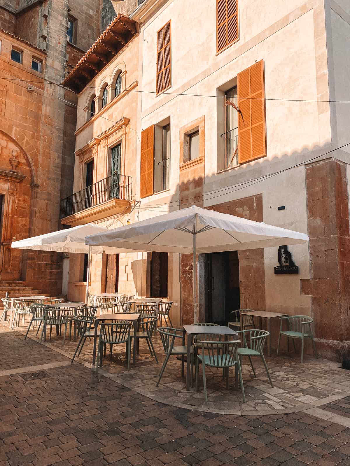 A cobblestone street with a cafe with umbrellas and blue chairs