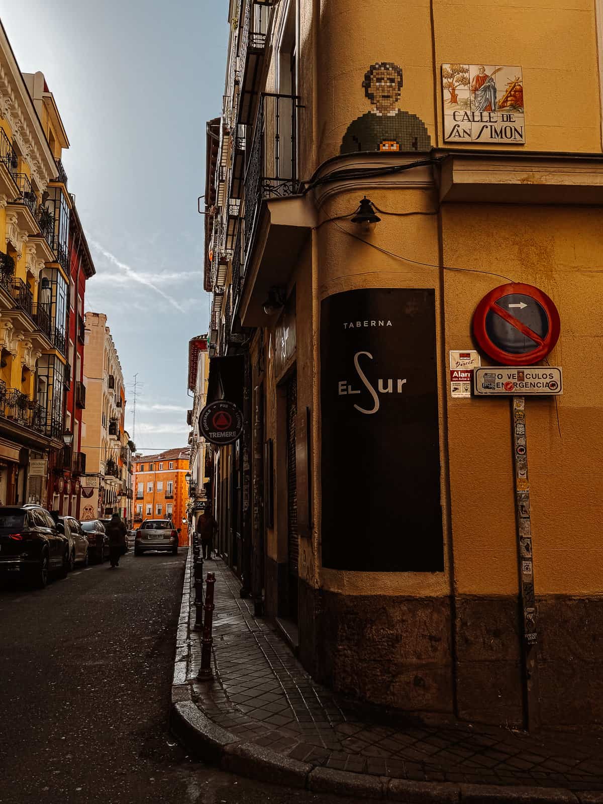 Narrow cobblestone street in a European city with traditional architecture, featuring the entrance to 'Taberna El Sur', under a sign with a no entry except for emergency vehicles