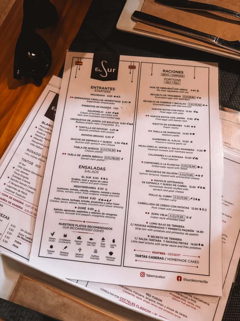 Menu of 'Taberna El Sur' displaying an assortment of Spanish cuisine including 'Empanadas', 'Tortilla de Patatas', 'Pimientos de Padrón', and various salads and meat dishes