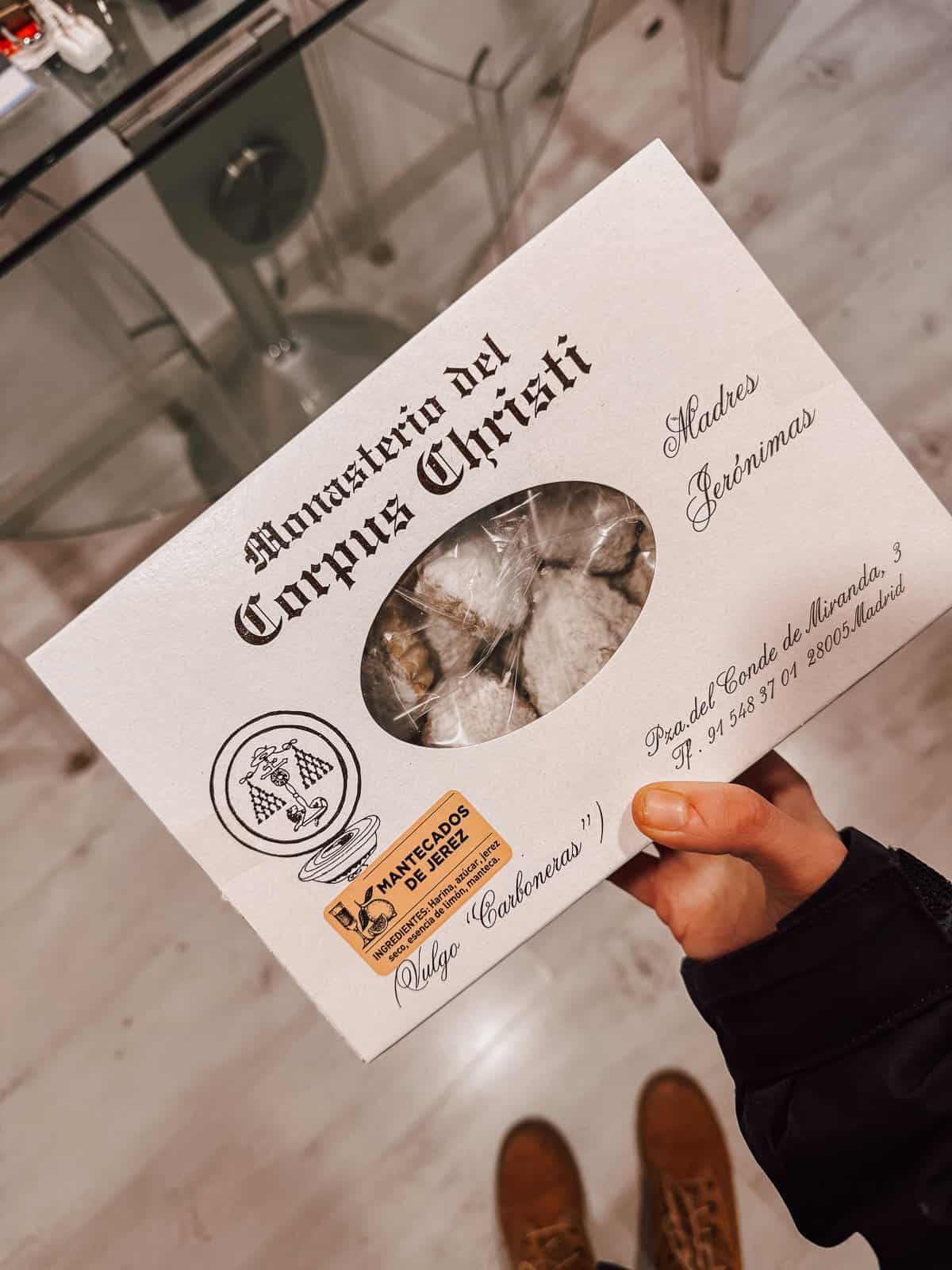 A person holds a box of 'Mantecados de Erez' from Monasterio del Corpus Christi, showcasing the convent's traditional Spanish cookies, with the name 'Madres Jerónimas' inscribed, offering a taste of local religious artisanal baking.