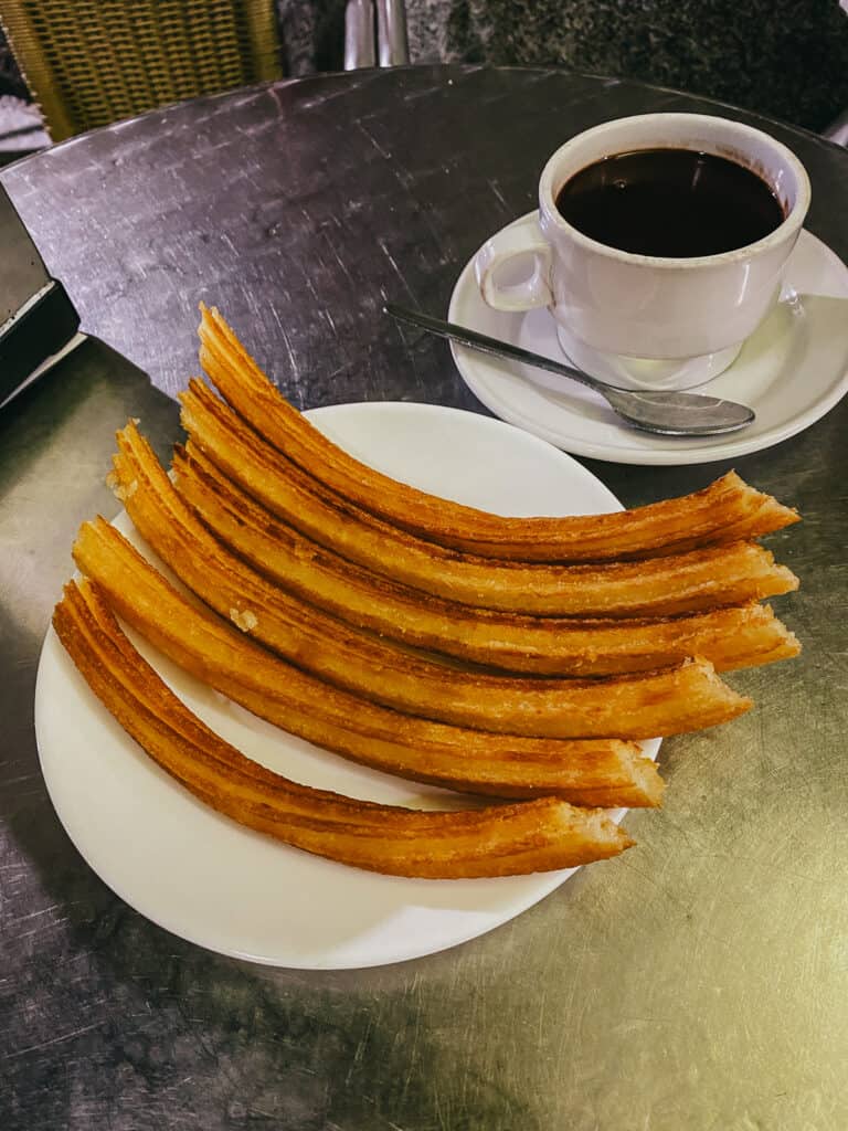 5 Spanish churros on a plate with a cup of melted chocolate