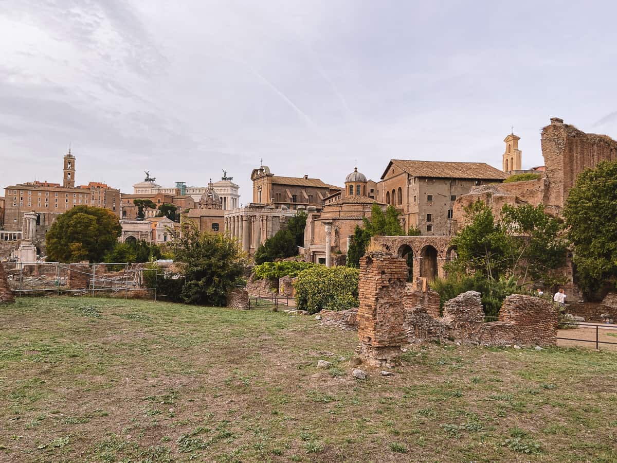 The ancient Roman Forum ruins in Rome, with its timeless columns and arches set against a backdrop of modern buildings, capturing the historical layers that define the Eternal City.