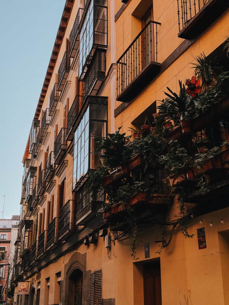 Traditional European architecture with rows of balconies filled with lush green plants, under a clear blue sky, showcasing urban residential beauty in a historic district.