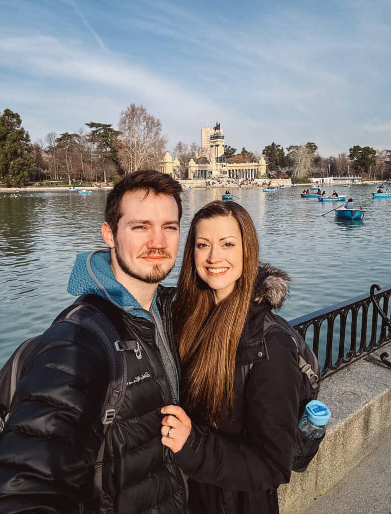 A joyful couple sitting on the edge of a fountain at Plaza Mayor in Madrid, the iconic red façades of the surrounding buildings framing their relaxed, contented pose.
