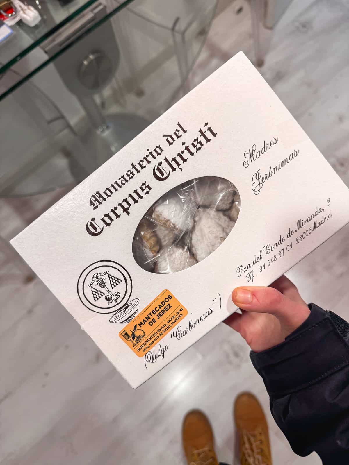 Hand holding a box labeled 'Monasterio del Corpus Christi Madres Jerónimas' filled with traditional 'Mantecados de Jerez', a Spanish shortbread.