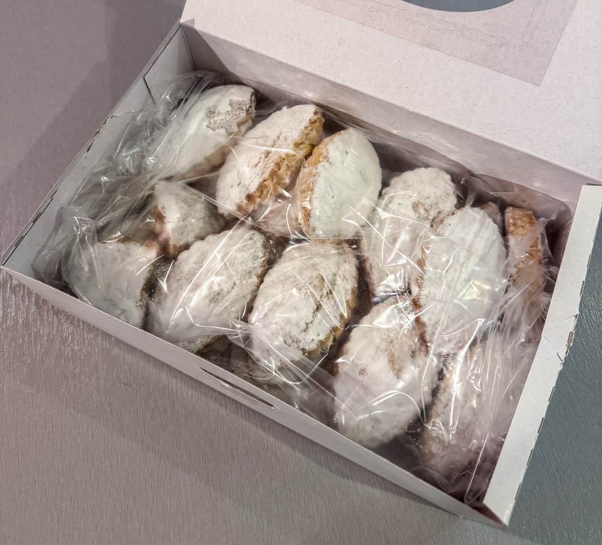 A box of assorted Spanish pastries, including 'Mantecados de Jerez', visible through a circular window in the box, set against a modern shop backdrop.