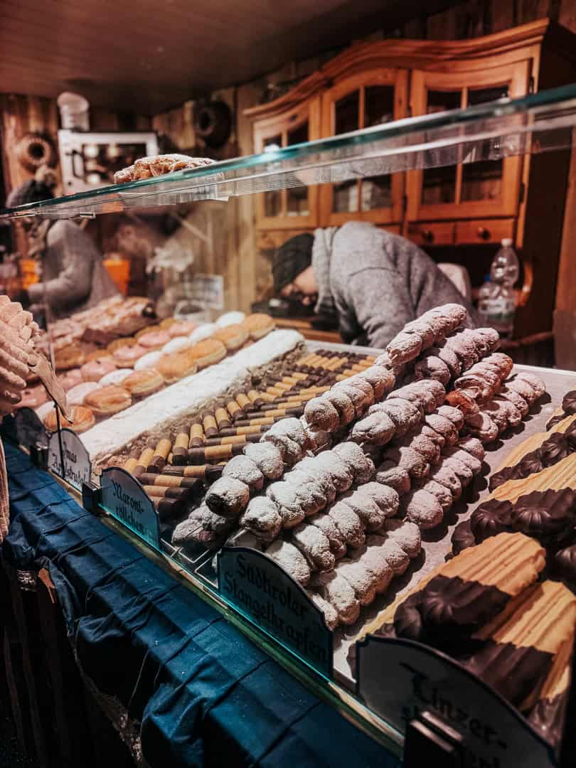 An array of traditional Christmas cookies and sweets neatly arranged in a Viennese market booth, with confections like macarons and Linzer cookies invitingly displayed.