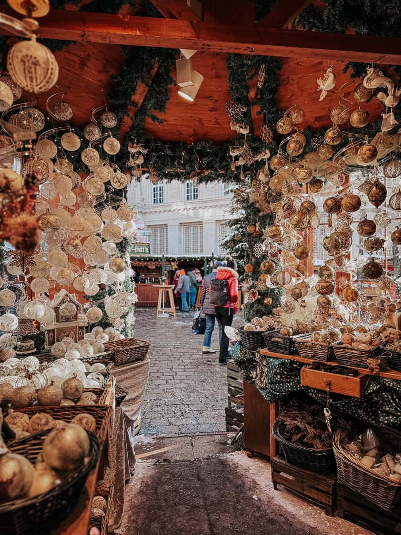 An entrance to a Viennese courtyard during Christmas, with a richly decorated tree and statue, as a person in winter clothing looks upward, captivated by the setting.