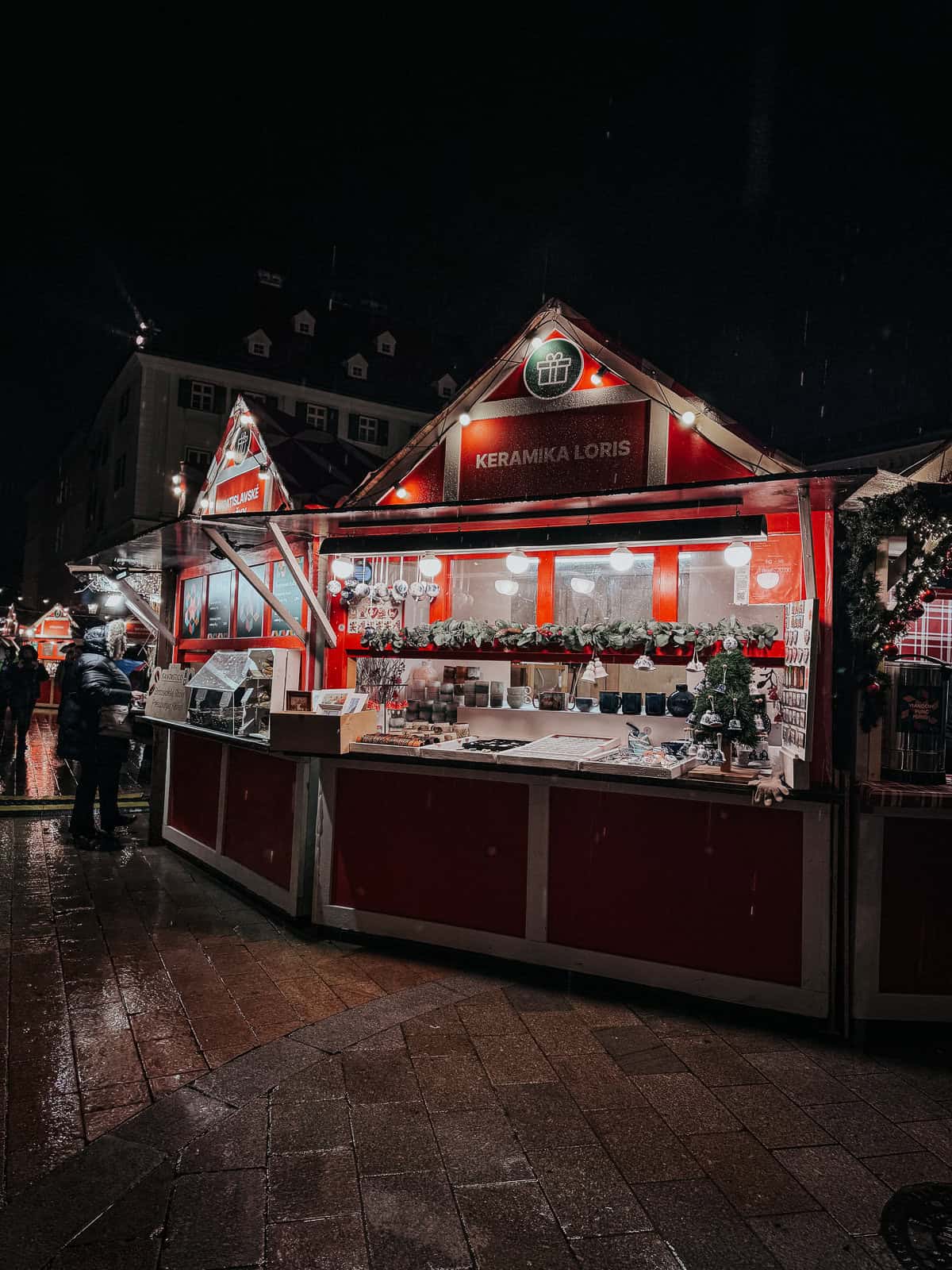 A night market stall brightly lit with red décor, displaying a variety of ceramic goods and festive lights.