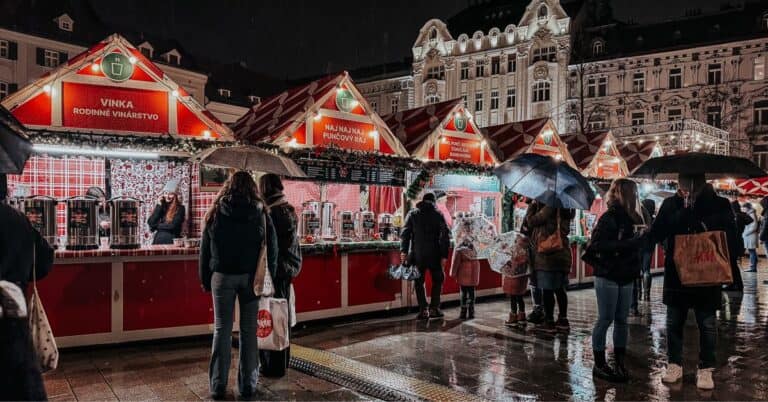 A bustling night market in Bratislava with festive lighting and rain-soaked pavements, people shopping under umbrellas.