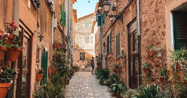 a narrow stone lane with brown stone buildings and lots of flowers