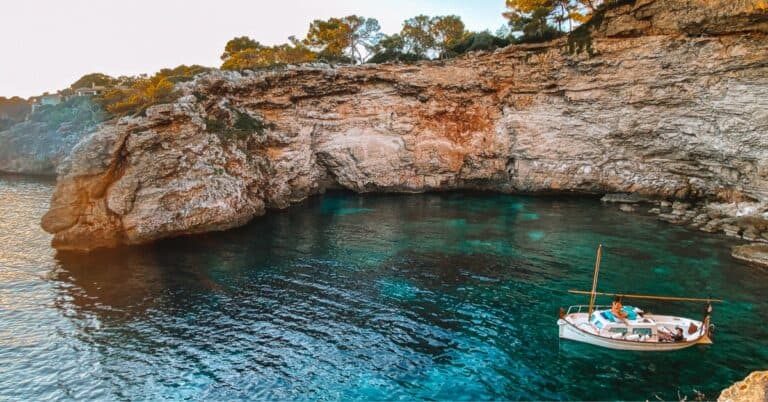 a catamaran in a cover with a rocky cliff and bright blue water in Mallorca