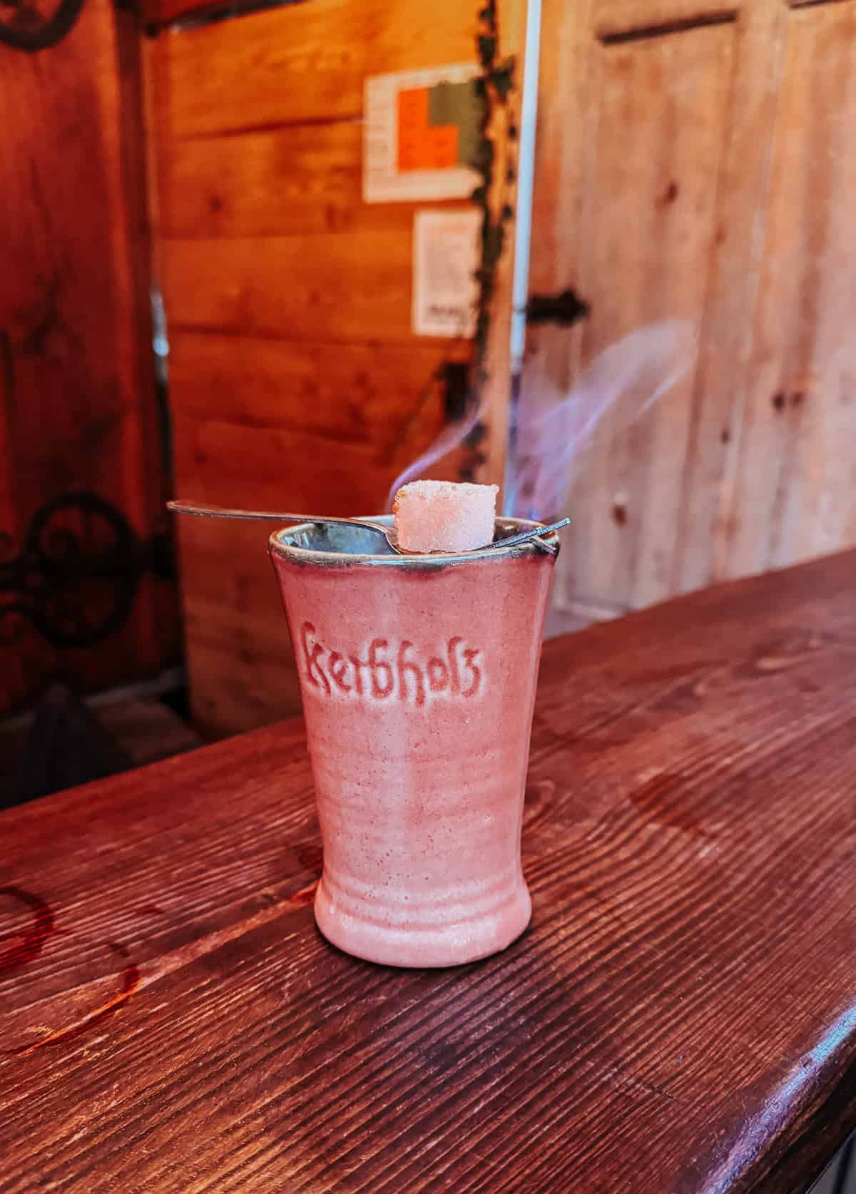 a pink mug of Feuerzangenbowle at a Christmas market with a sugar cube lit on fire overnight