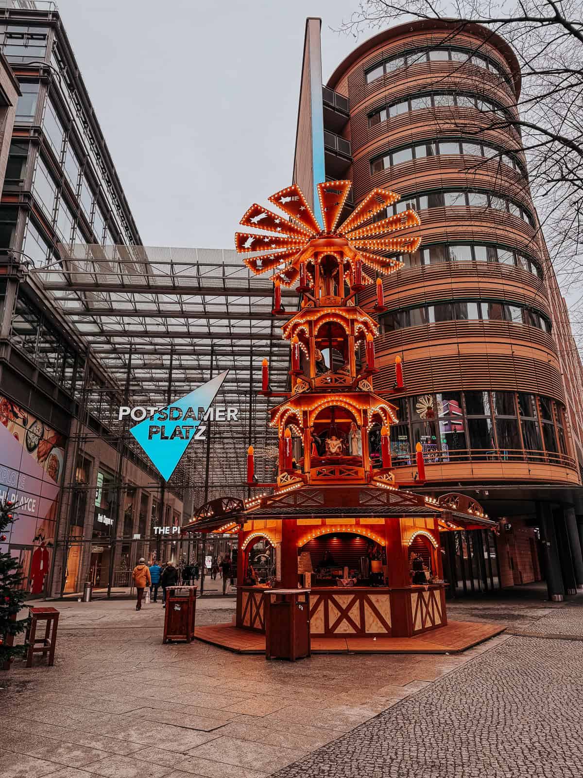 A brightly lit Christmas-themed carousel at an urban square, surrounded by modern buildings. The carousel features elaborate decorations and festive lights, creating a joyous holiday atmosphere.