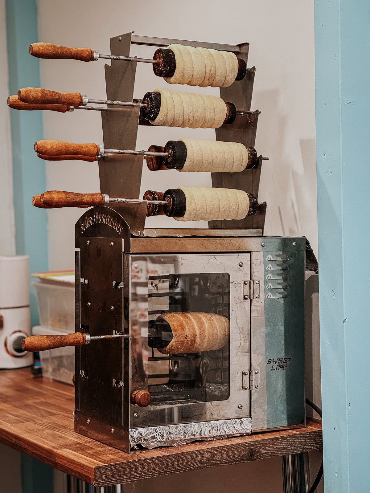 Chimney cakes being baked on wooden spits in a traditional oven, with the golden-brown cakes ready to be served.