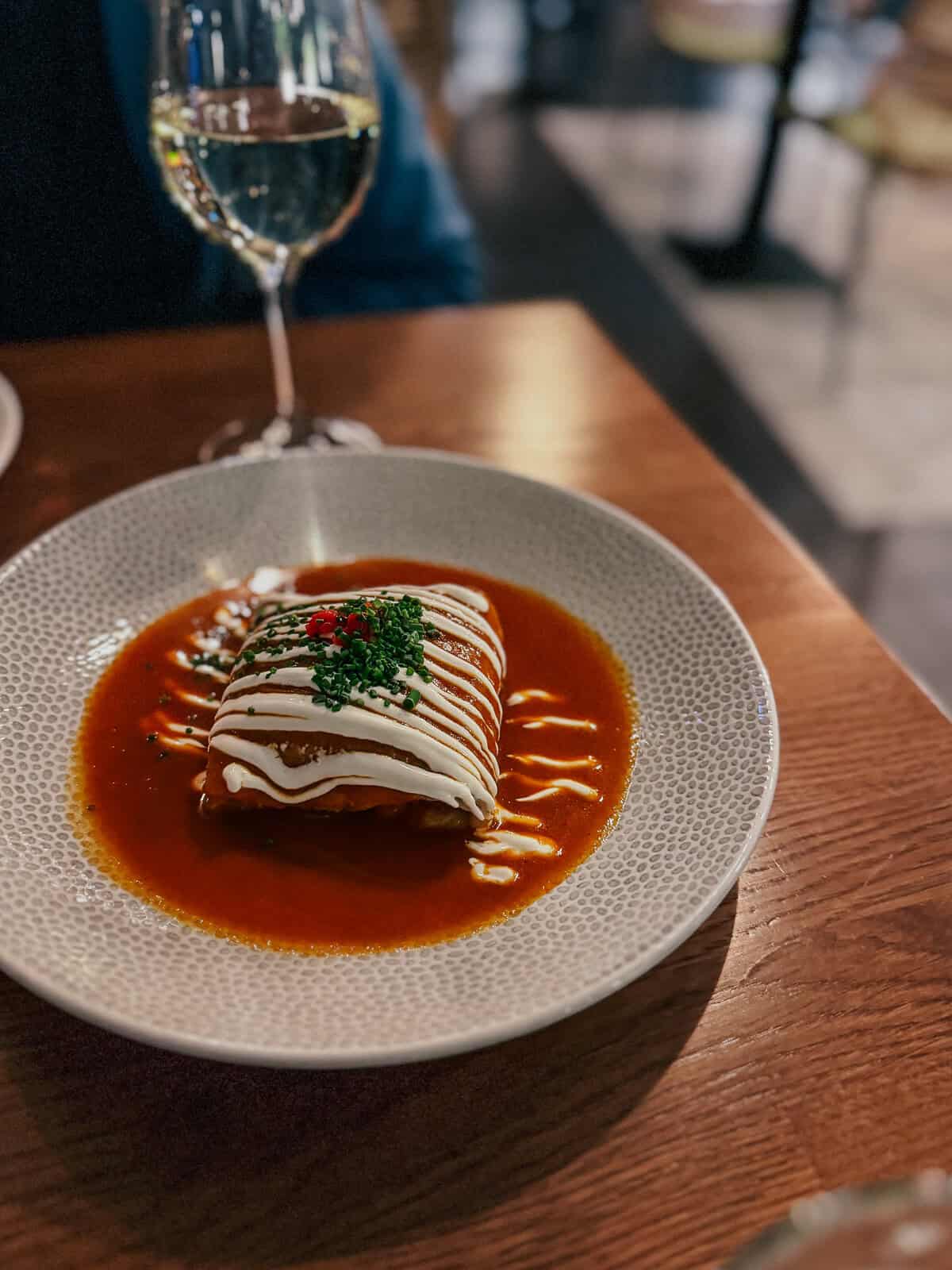 A dish of Hortobágyi crepe served in a bowl with a rich sauce, topped with sour cream and garnished with green herbs.