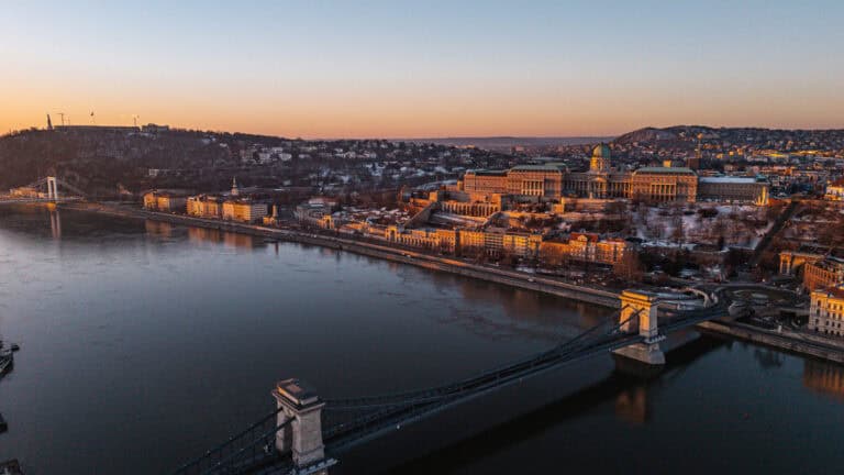 Aerial view of the Hungarian Parliament Building at sunrise, situated along the Danube River with the cityscape of Budapest in the background
