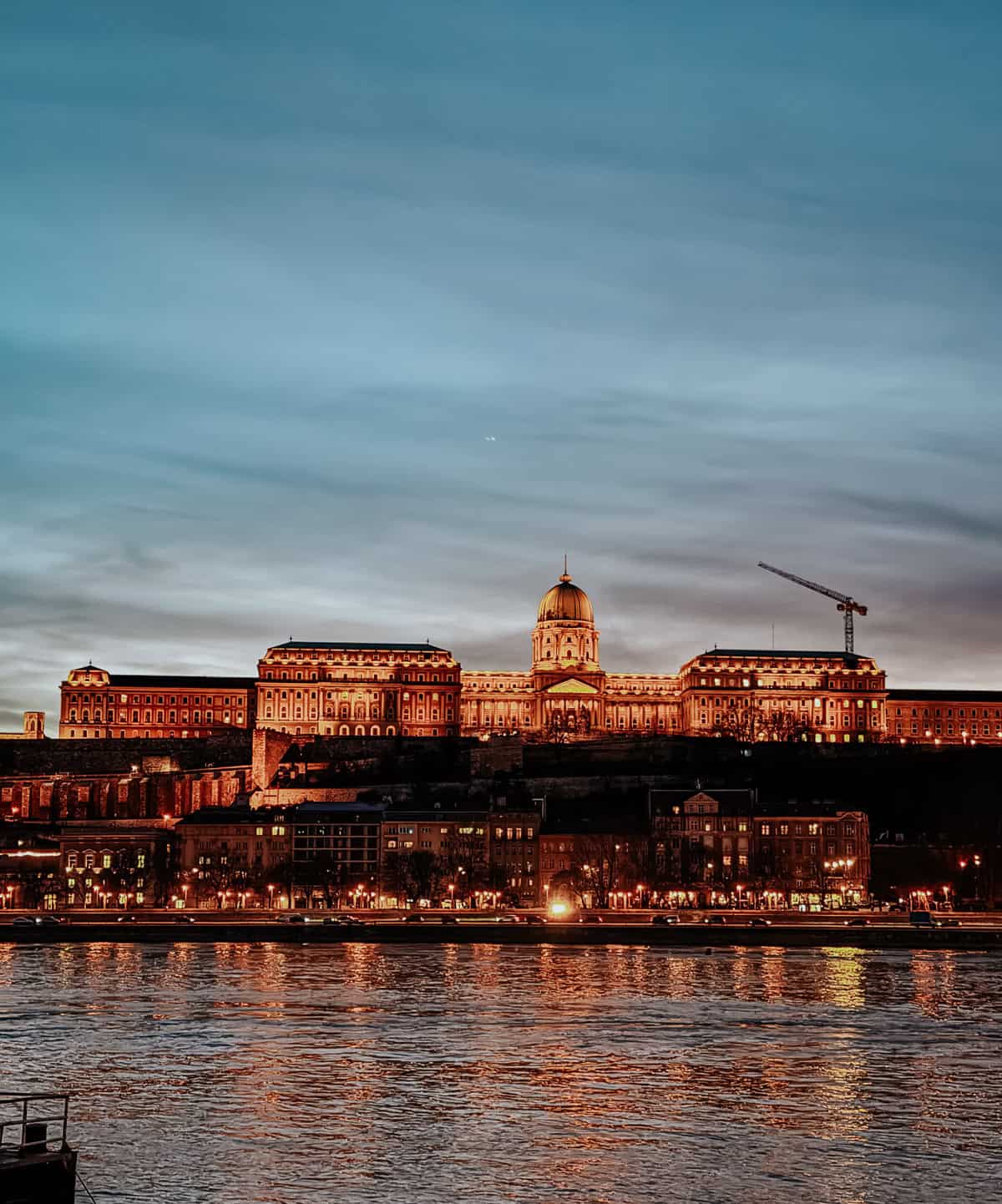 The Buda Castle in Budapest lit up beautifully at night, with its reflection shimmering on the Danube River.