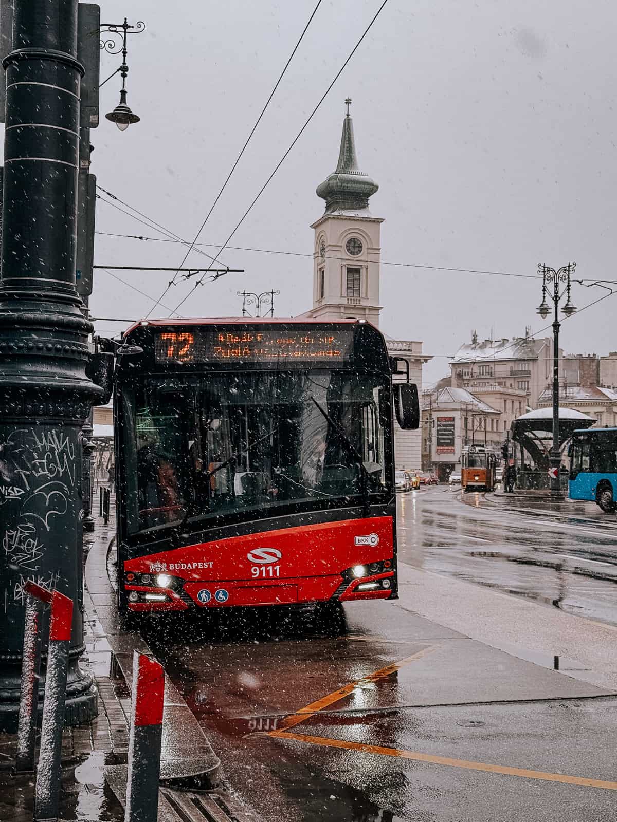 a red bus in budapest crossing a bridge in the snow