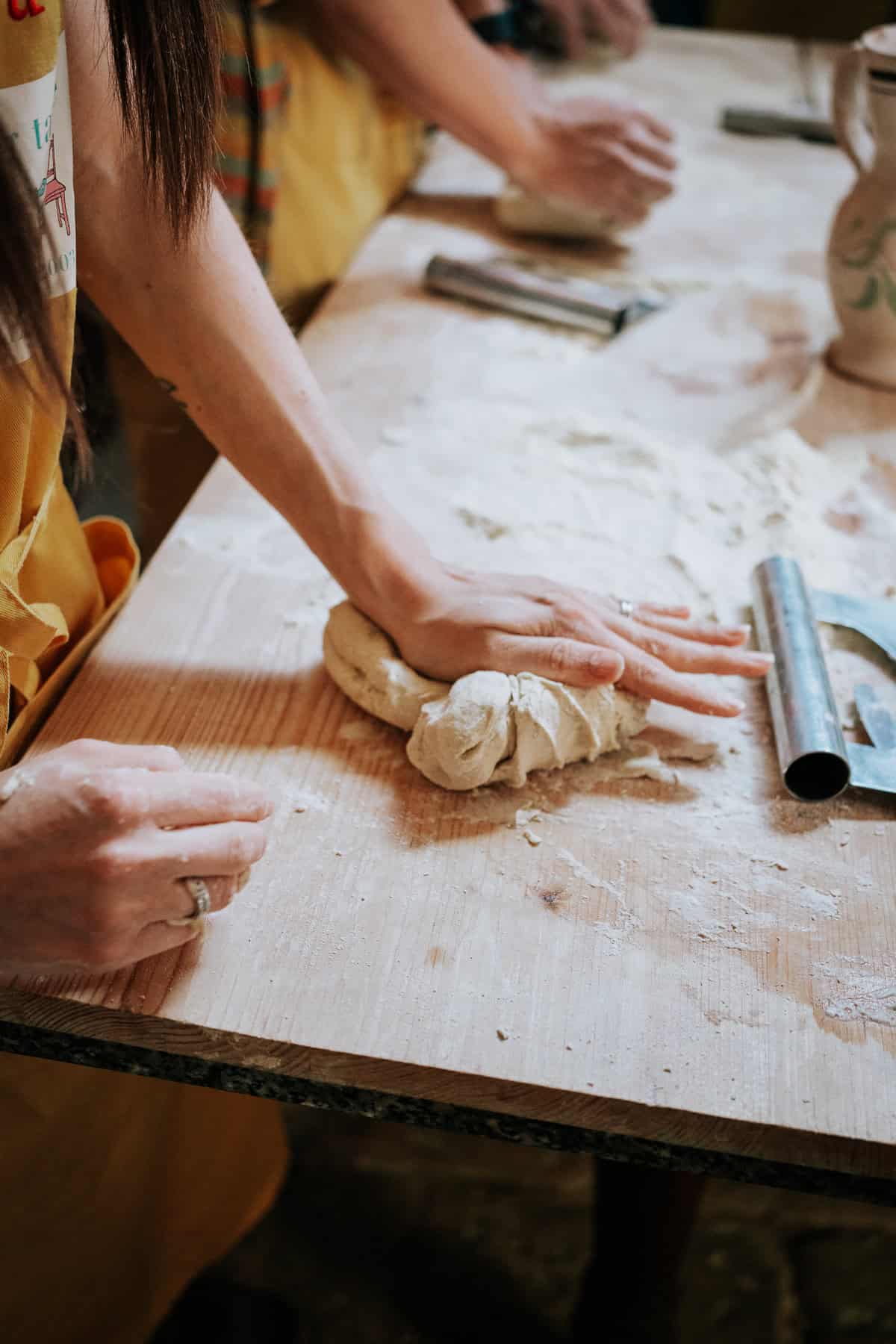 A close-up of hands kneading dough on a floured wooden surface during a pasta-making workshop in Lecce, Italy. Various tools and ingredients surround the workspace, emphasizing the artisanal process.