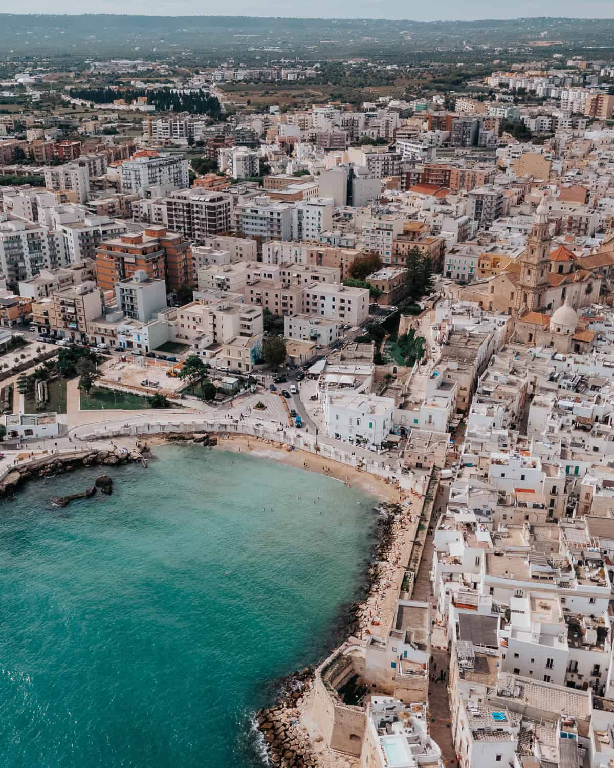 A stunning aerial view of Monopoli, Italy, showcasing its historic whitewashed buildings, vibrant harbor, and deep blue Adriatic coastline.