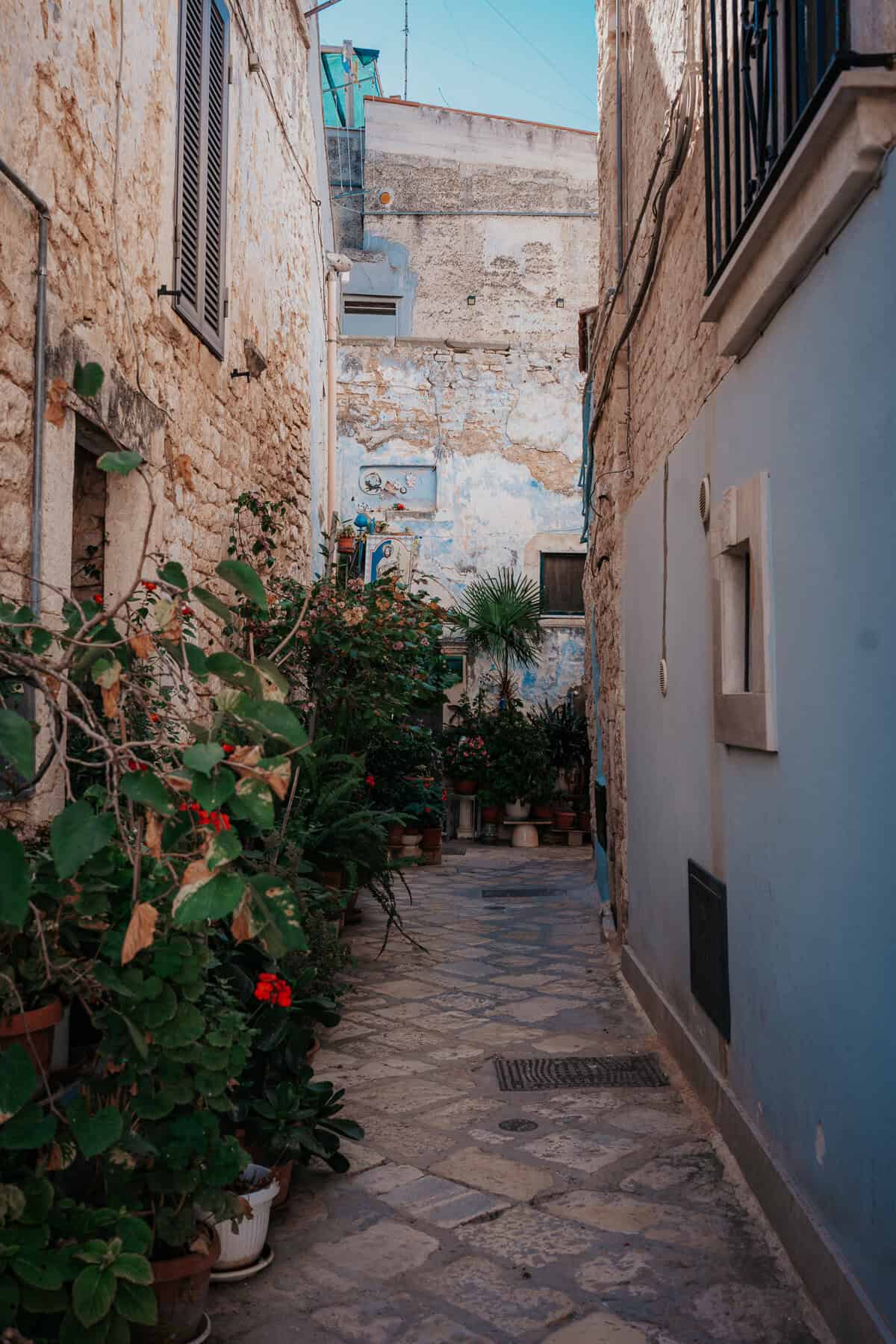 A picturesque alley in Casamassima, Italy, with whitewashed buildings, rustic stone streets, and a small historic bell tower in the background.