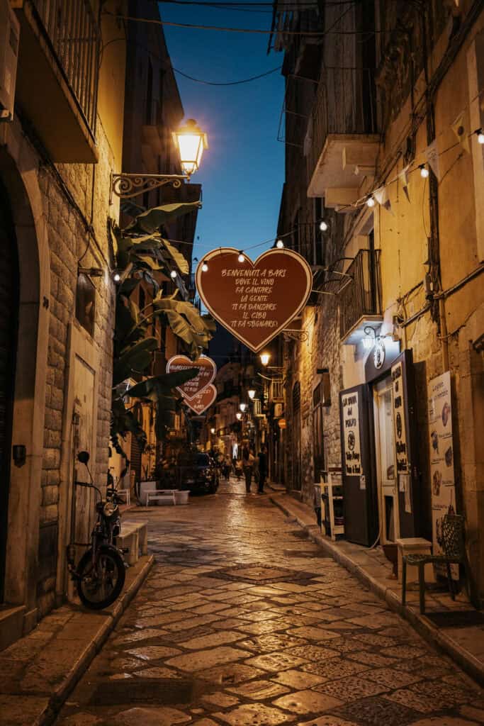 A serene night view of Bari, Italy, with warm golden streetlights reflecting off the cobblestone streets and historic architecture