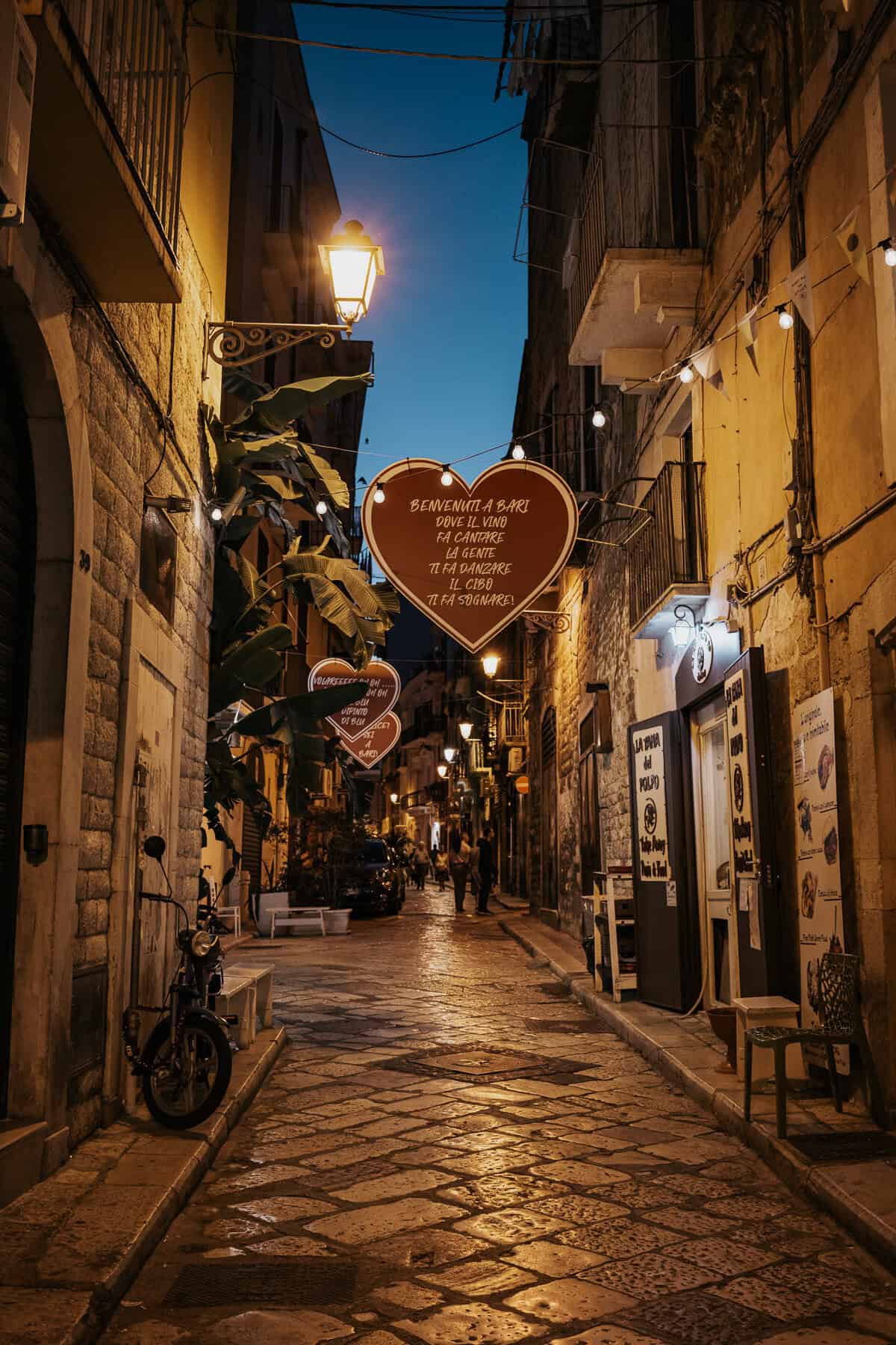 A serene night view of Bari, Italy, with warm golden streetlights reflecting off the cobblestone streets and historic architecture