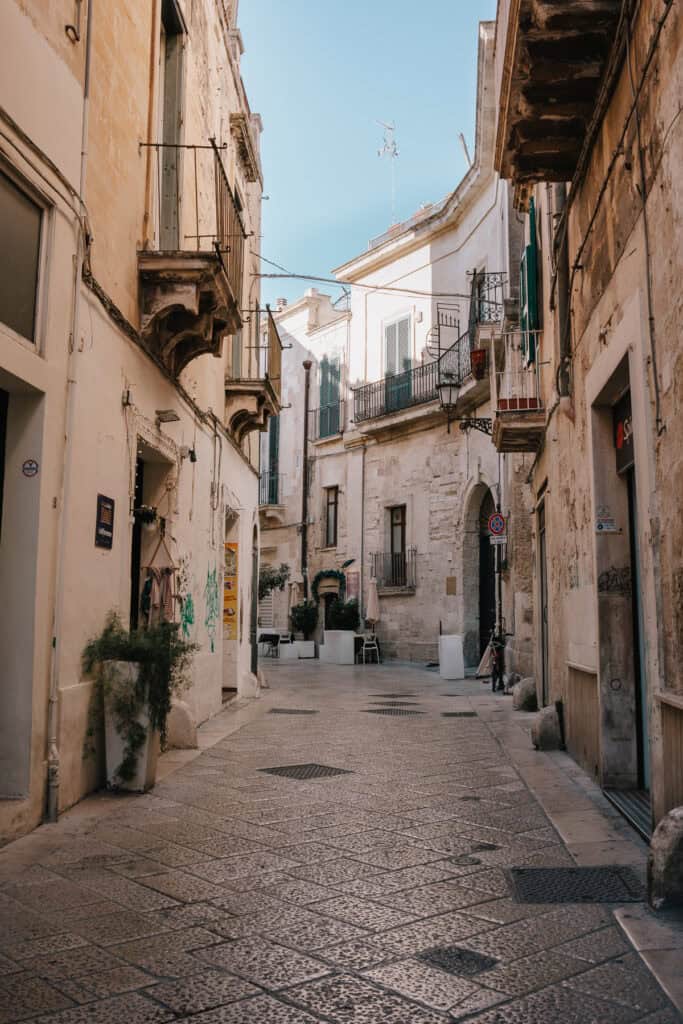 A beautifully preserved old town street in Lecce, Italy, lined with historic baroque buildings, ornate balconies, and charming cafés.