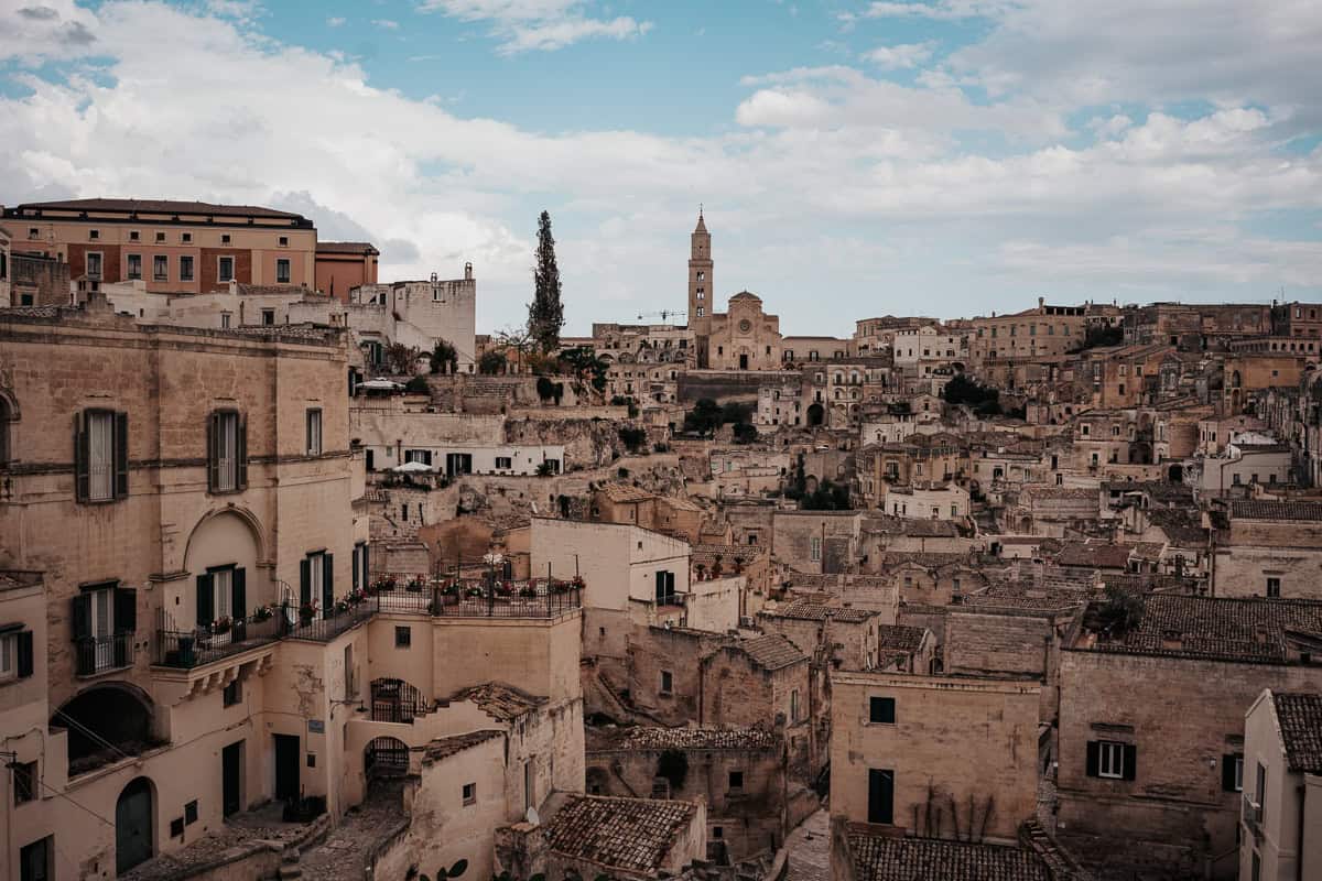 A panoramic view of Matera, Italy, showcasing the iconic Sassi cave dwellings, ancient stone houses, and the historic cathedral standing tall over the city