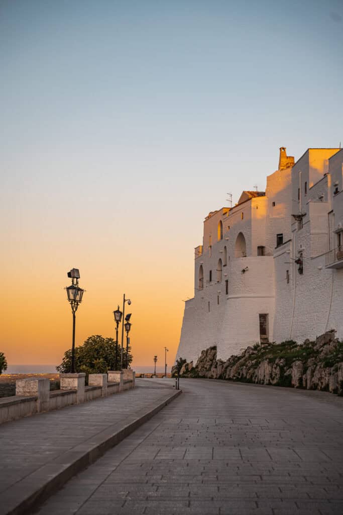 A stunning sunset in Ostuni, Italy, with the golden light illuminating the white buildings perched on a hilltop overlooking the sea.