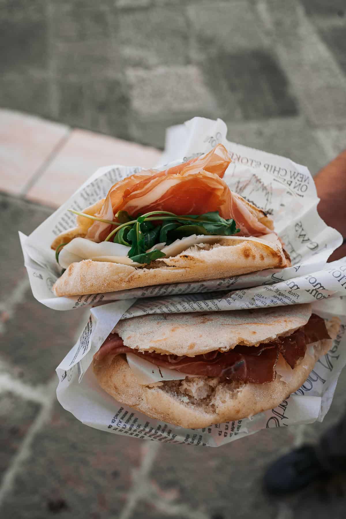 A fresh puccia sandwich from Puglia, Italy, filled with cured meats, fresh arugula, and local cheeses, wrapped in rustic paper.