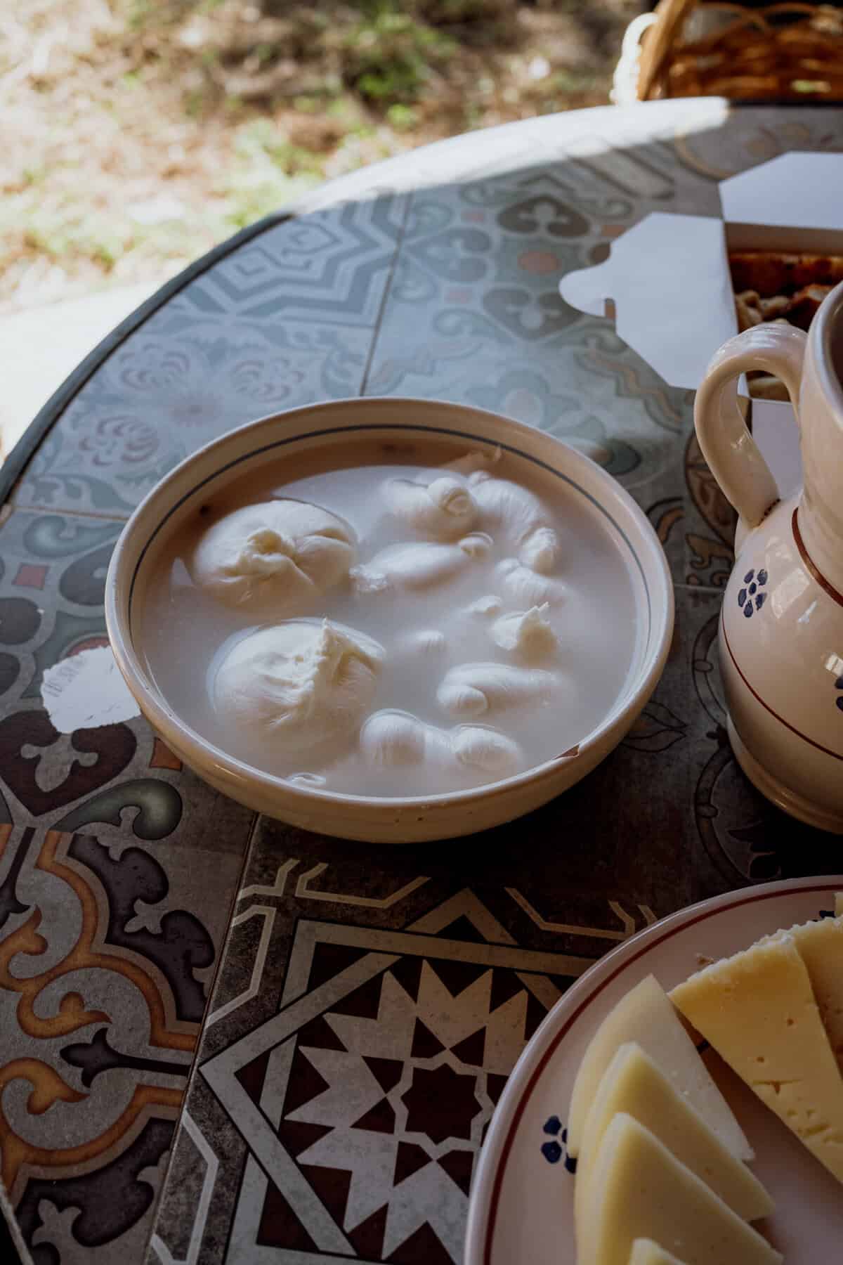 Close-up of a ceramic bowl filled with fresh burrata balls soaking in milky brine, highlighting their soft, pillowy texture.