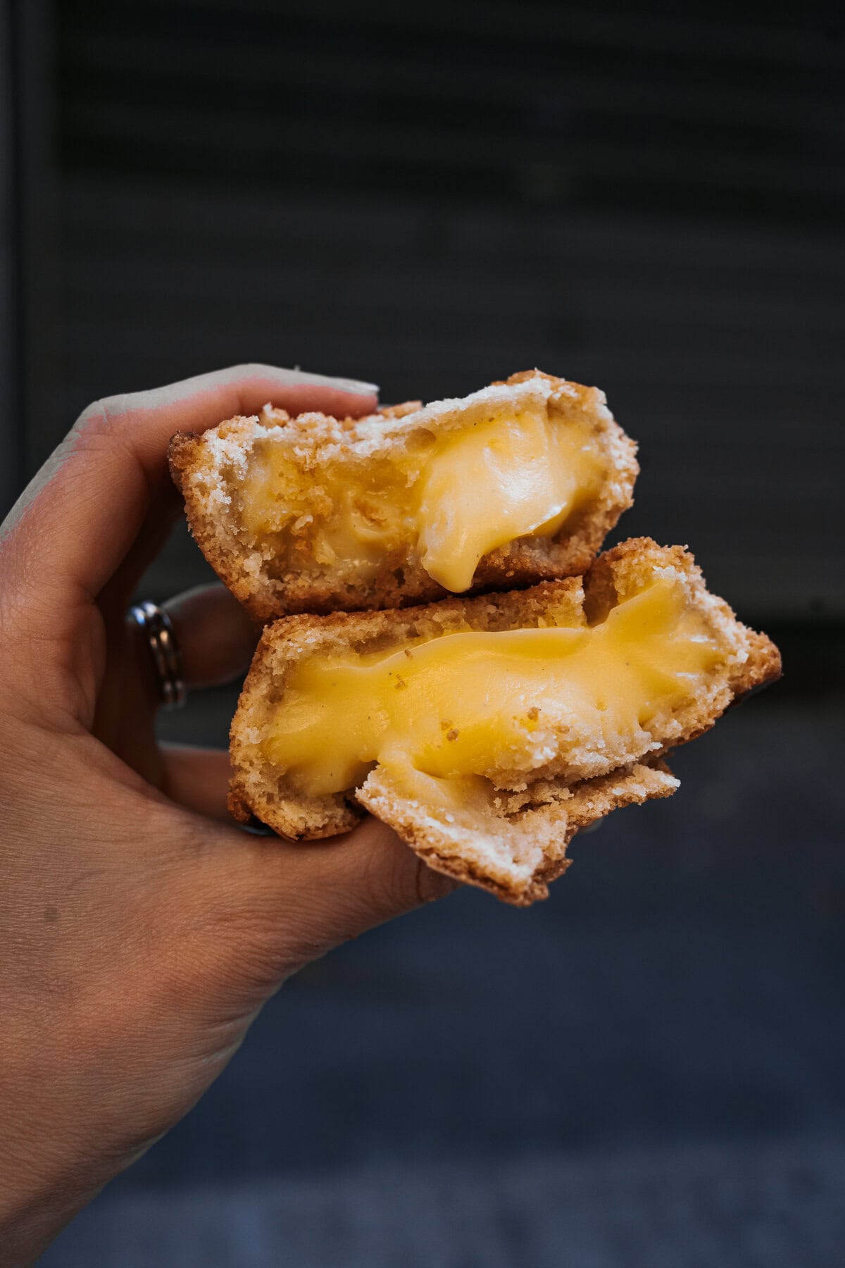 A hand holds a split-open pasticciotto pastry, revealing a rich, gooey yellow custard filling inside a golden, crumbly shell.