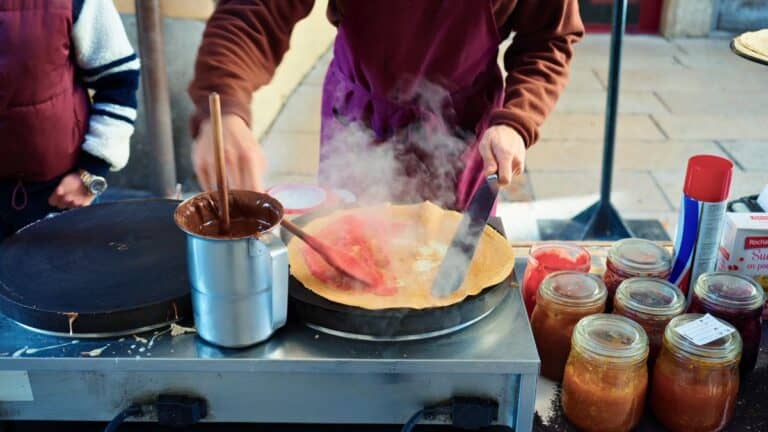 Street vendor cooking a French crêpe filled with pink praline sugar on a hot griddle in Lyon