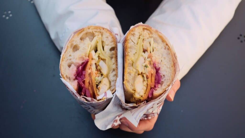 Cross-section of a French baguette sandwich with chicken, cheese, pickled vegetables, and sauce