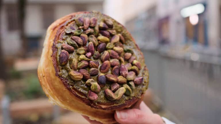 Pistachio-filled pastry roll in Lyon, topped with whole pistachios and baked into a flaky, golden croissant-style dough
