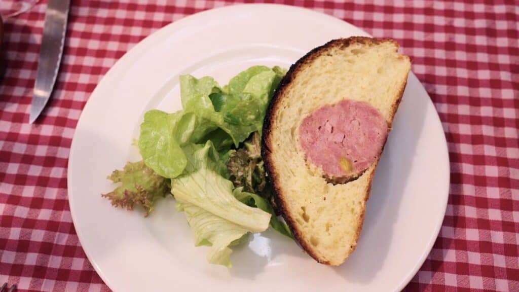 Slice of saucisson brioche with sausage baked inside buttery bread, served with salad