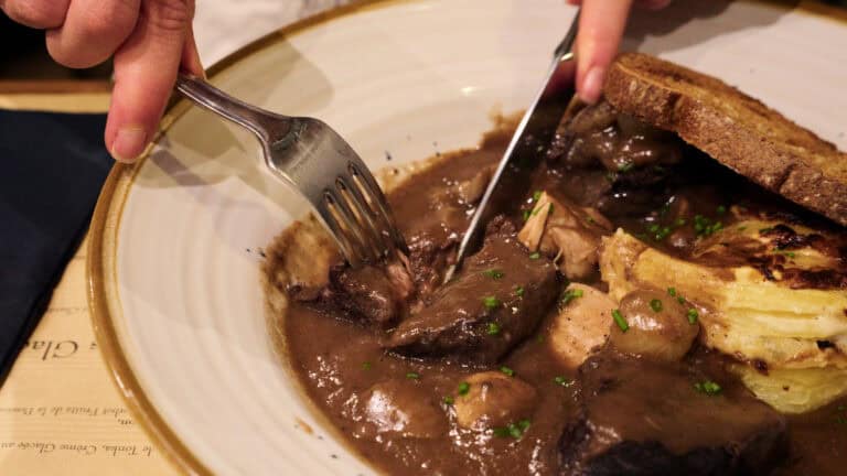 Close-up of fork cutting into slow-braised French beef stew with mushrooms and rich gravy