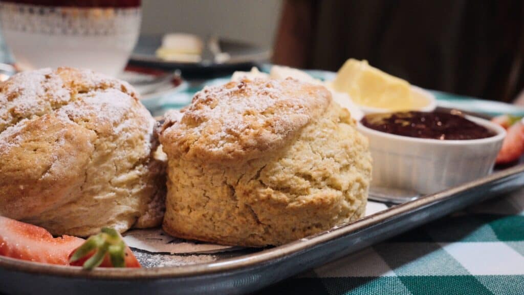 Freshly baked scones dusted with powdered sugar are served with jam and clotted cream on a tray in a cozy café. This weekend in the Cotswolds moment highlights a classic afternoon tea experience.