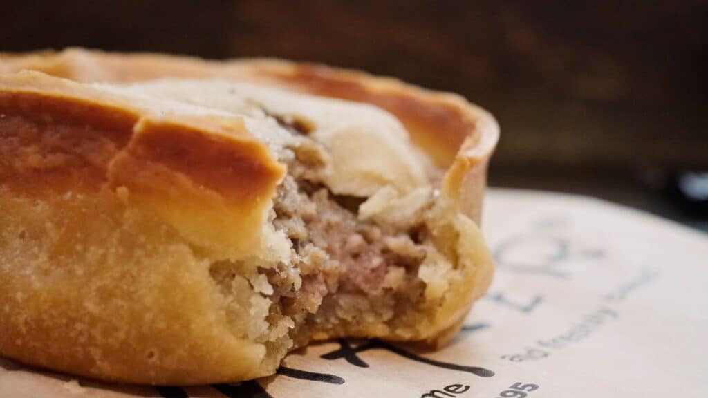 Close up of a traditional meat pie with flaky golden crust broken open to reveal minced filling inside. The hearty pie is a staple of traditional Scottish food found in bakeries and pubs.