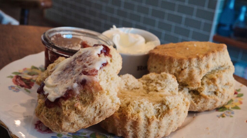 Freshly baked scones served with jam and cream on a floral plate in a tea setting. This traditional English food treat is part of a classic afternoon tea experience.