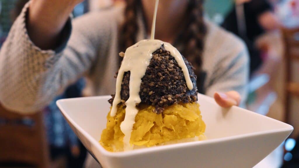 Plate of haggis served over mashed neeps and tatties with creamy sauce being poured on top. The iconic dish of haggis with turnips and potatoes is one of the most recognizable traditional Scottish foods.