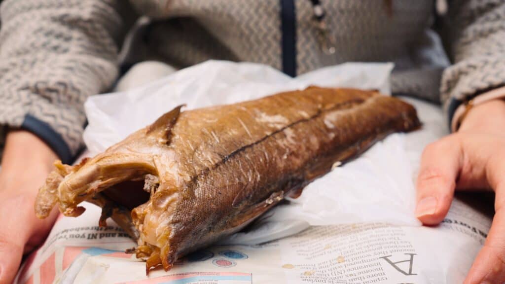 Whole smoked fish resting on paper while a person holds it on their lap. Smoked fish like kippers are a traditional Scottish seafood specialty.